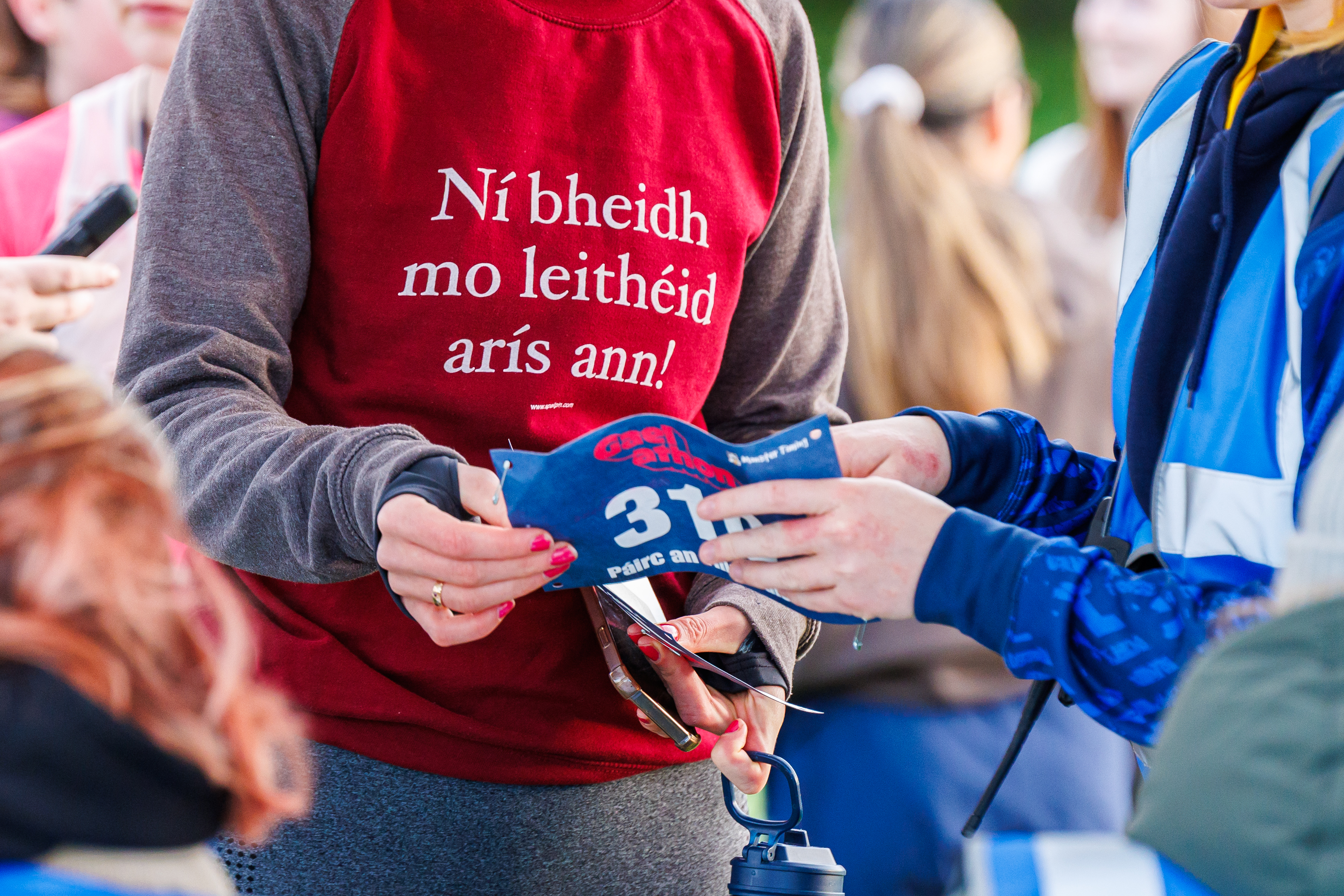 A Gaelathon participant holds a race bib printed with Irish-language event branding